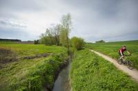 fietser rijdt op wegje naast een beek, in een groen landschap